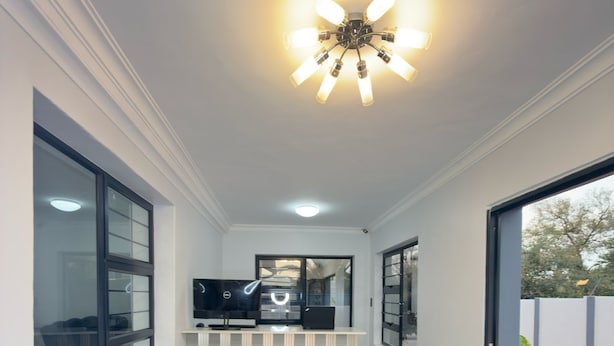 A modern living room with a sofa, a television, and a ceiling light fixture. - Cozy Villa Lodge (Edenvale)