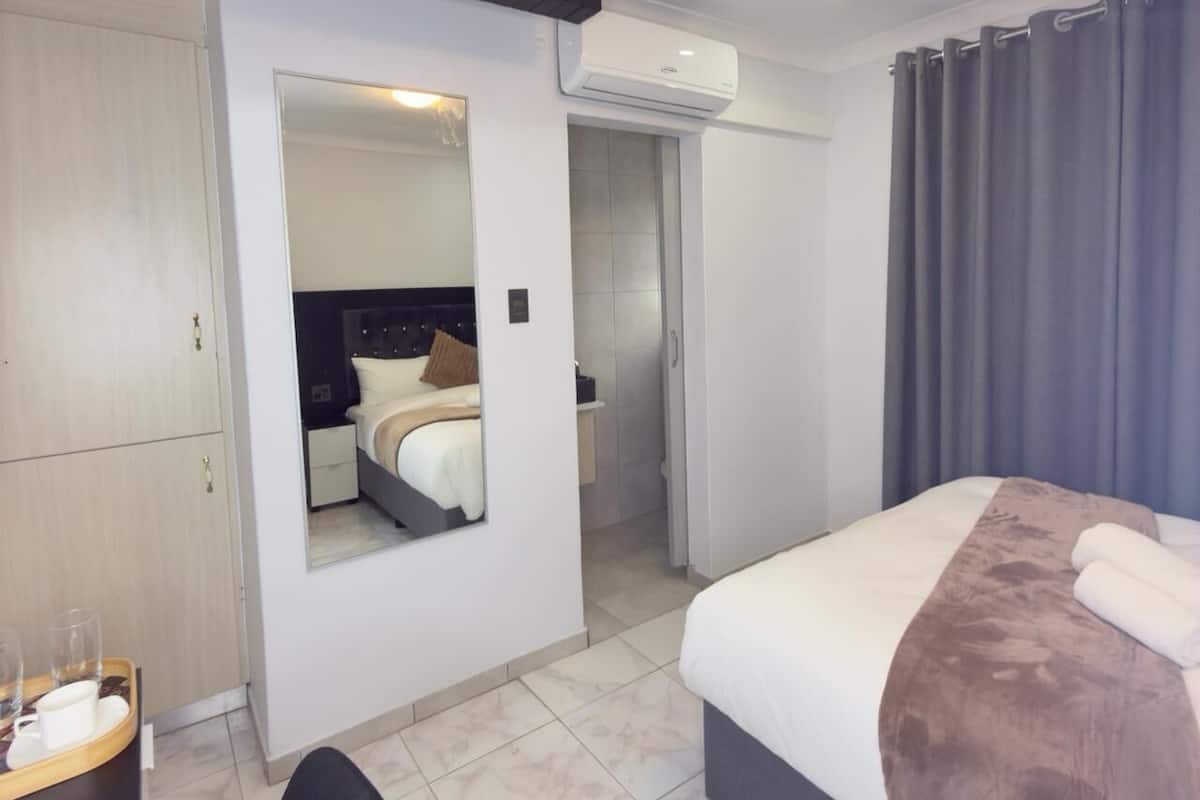 Una habitación de hotel moderna con cama, armario, espejo, equipo de aire acondicionado y puerta de baño.