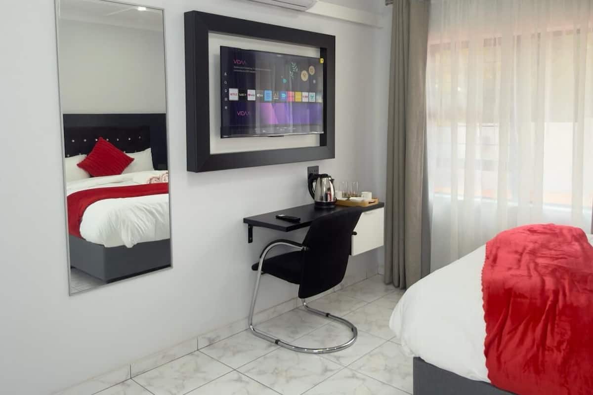 Una habitación de hotel moderna con cama, escritorio, silla, espejo grande y televisor instalado en la pared.