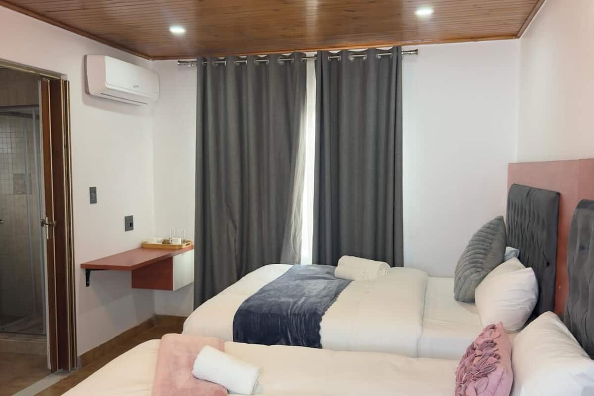 Un dormitorio con dos camas, techo de madera, unidad de aire acondicionado, ventana con cortinas y un estante con objetos.