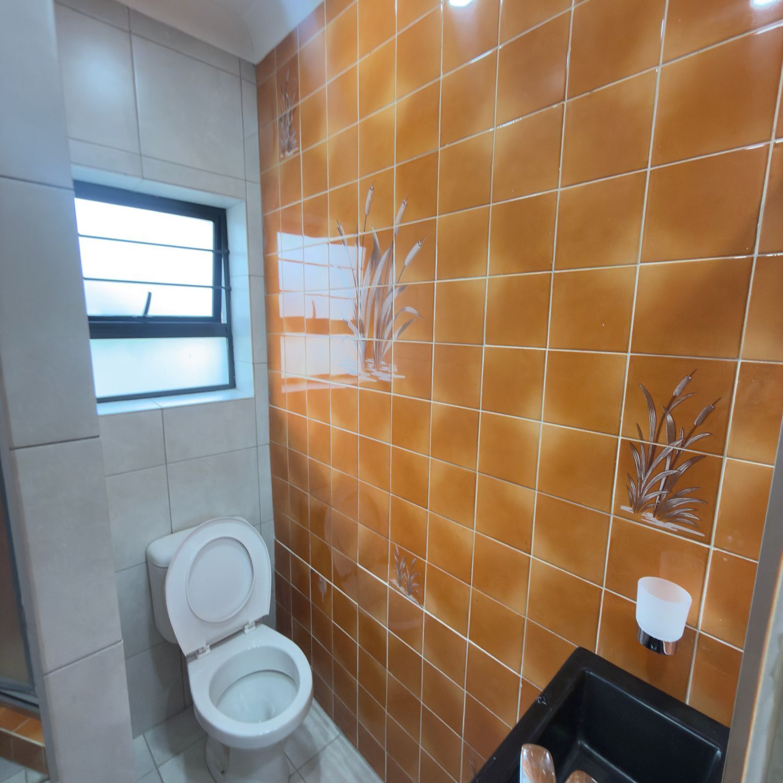 A bathroom with a toilet, a window, and a wall with a plant design.