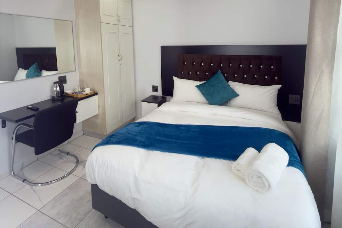 Una habitación de hotel con cama, escritorio, armario, espejo y mesita de noche.