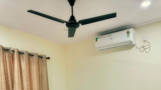 Ein Schlafzimmer mit einem Bett, einem Deckenventilator, einer Klimaanlage und einem Vorhang.