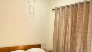 Ein ordentlich bezogenes Bett mit weißen Leinen und Handtüchern, ein Holz-Kopfteil, ein Nachttisch mit Lampe sowie ein gemustertes Vorhang.