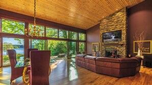 A modern living room with a stone fireplace, a large TV, and a view of the outdoors. - An Artist's Story: A Private Sanctuary-devoted to art and quiet poetry..... (Logan)