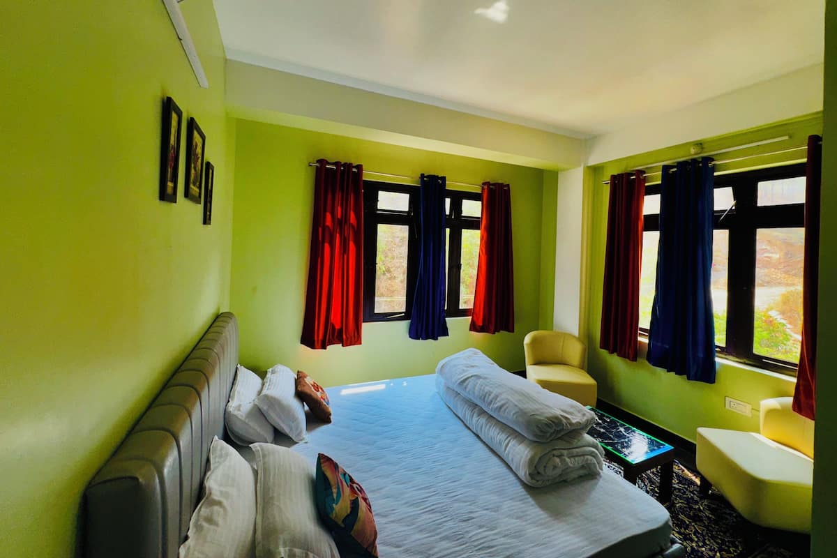 A hotel room with a bed, a chair, a table, and a window with curtains.