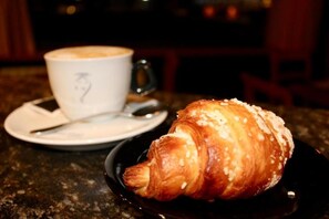 Un croissant sobre un plato negro con una taza de café en un platito.