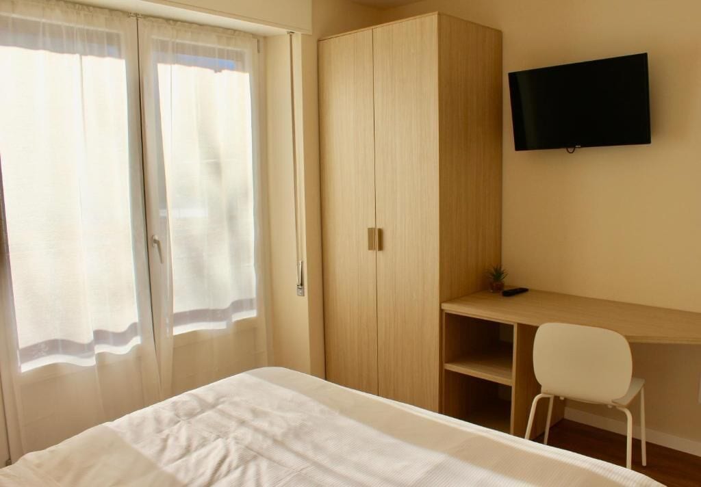 Una camera da letto con un letto, un armadio, una scrivania, una sedia e una TV a parete.