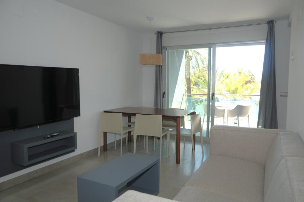 Una sala moderna con televisor de pantalla plana, una mesa de comedor con sillas, un sofá y un balcón con vistas.
