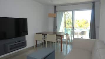 Una sala moderna con televisor de pantalla plana, una mesa de comedor con sillas, un sofá y un balcón con vistas.