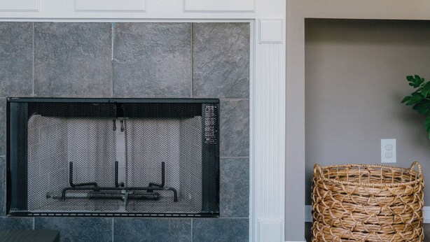 A fireplace with a stone surround, a woven basket, and a framed picture on the wall.