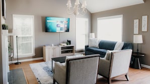 A living room with a flat-screen TV, a blue sofa, two armchairs, a coffee table, and a chandelier.
