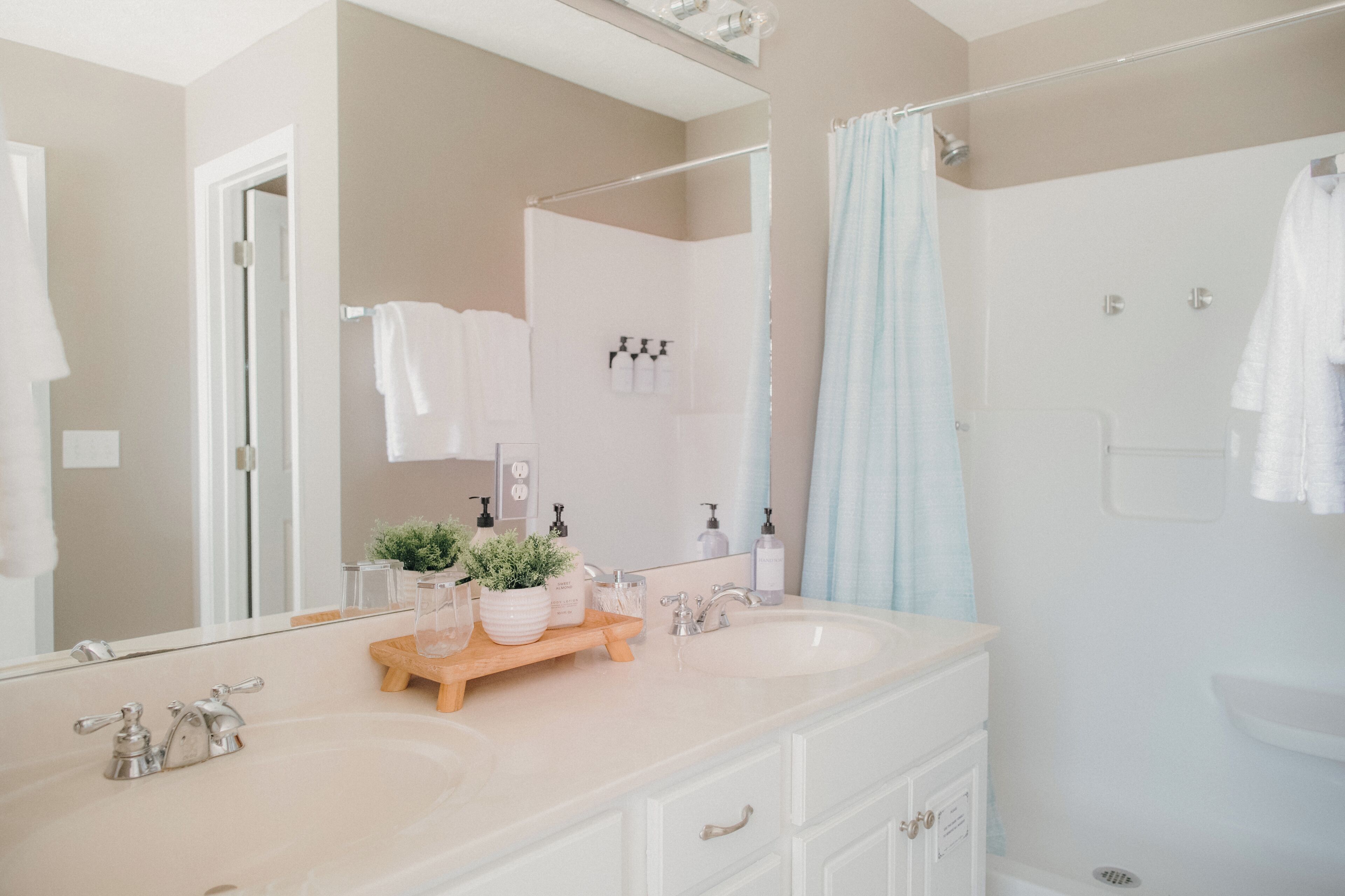 A bathroom with two sinks, a mirror, a shower, and a towel rack.