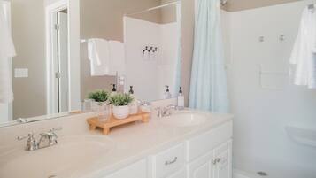 A bathroom with two sinks, a mirror, a shower, and a towel rack.