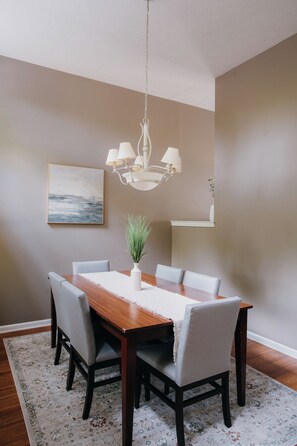 A dining room with a wooden table, six chairs, a chandelier, a painting, and a plant. - Copperfield Retreat 3BR | Pet-Friendly Escape (Montgomery)