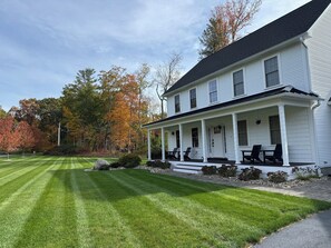 Une maison blanche à deux étages, dotée d’un porche, d’une pelouse bien entretenue et, en arrière-plan, d’arbres aux couleurs automnales.