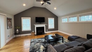 A spacious living room with a fireplace, a ceiling fan, and a large window.