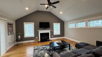 A spacious living room with a fireplace, a ceiling fan, and a large window.