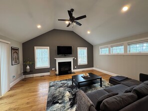 Un salon spacieux doté d’une cheminée, d’un ventilateur de plafond et d’une grande fenêtre.