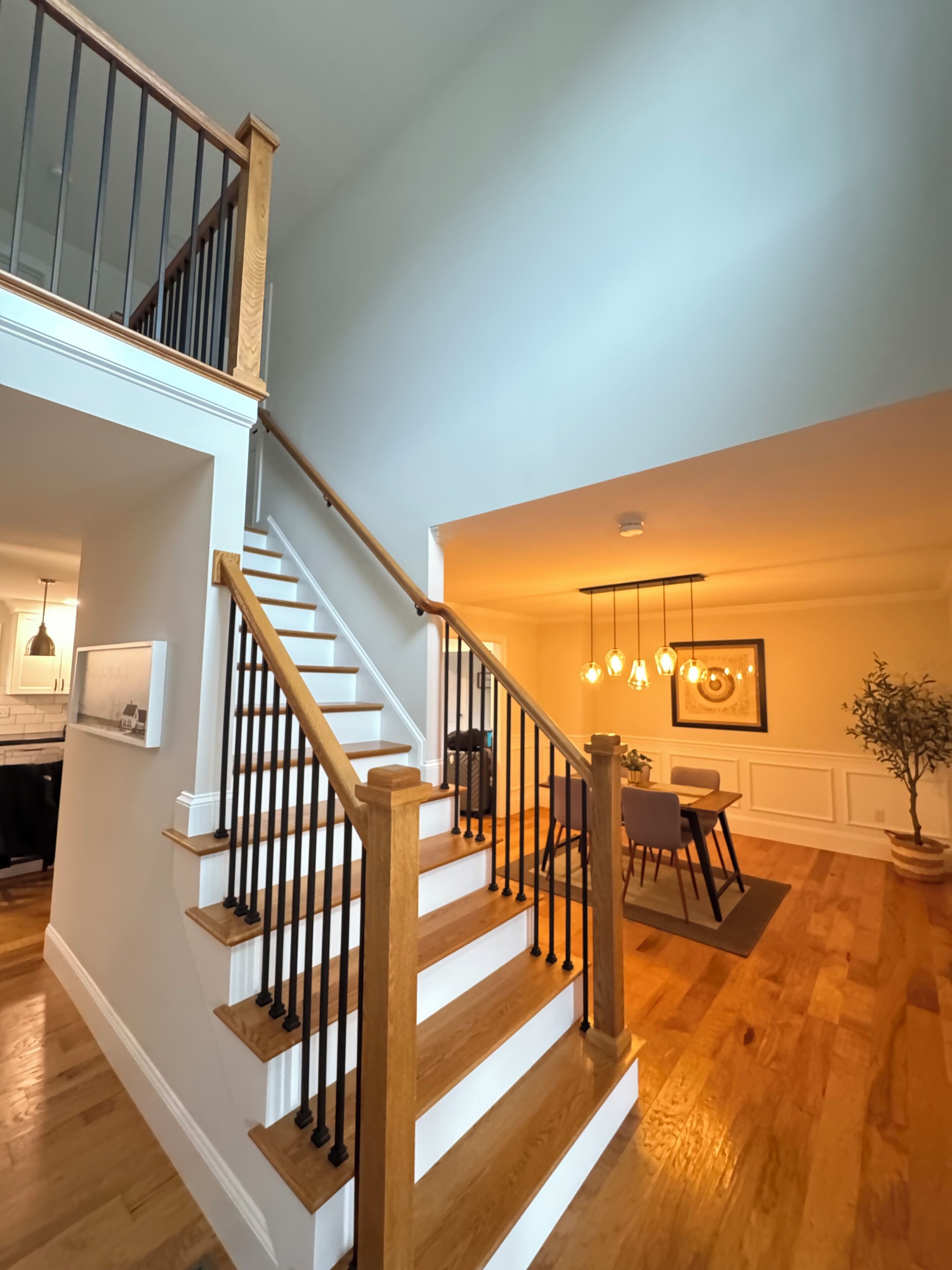 A staircase with wooden steps and black railings, leading to a dining area with a table and chairs.