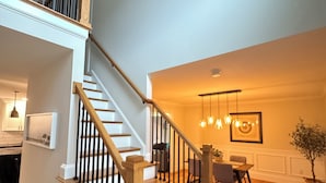A staircase with wooden steps and black railings, leading to a dining area with a table and chairs.