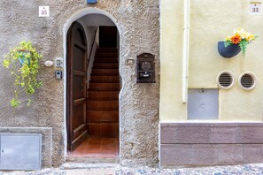 A stone building with a wooden staircase, a mailbox, and a flower pot. - Studio 'Domus Santa Barbara' with Wi-Fi (Alghero)
