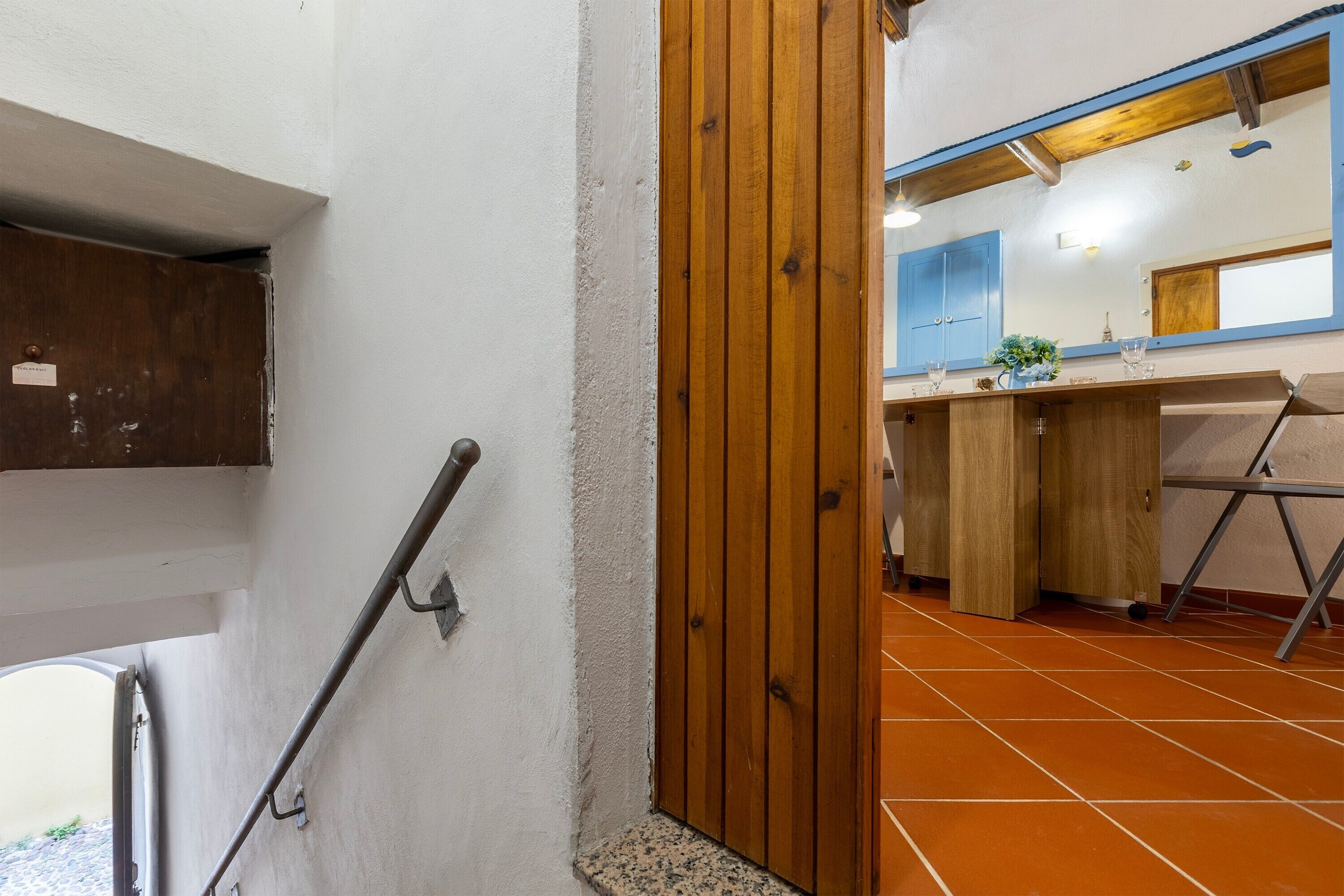 A bathroom with a wooden door, a sink with a mirror, and a tiled floor.