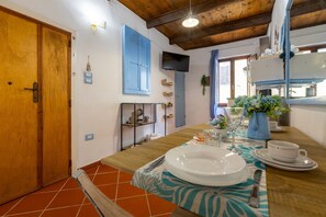 A dining area with a table set for two, a wooden door, a television mounted on the wall, and a kitchen area visible in the background. - Studio 'Domus Santa Barbara' with Wi-Fi (Alghero)