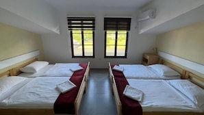 Una habitación con dos camas, una ventana, un aire acondicionado y una mesita de noche pequeña.
