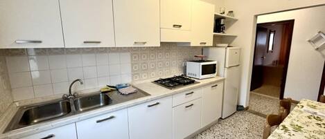 Une cuisine avec des armoires blanches, un évier en acier inoxydable, un four à micro-ondes et une cuisinière.