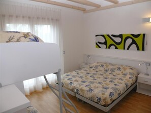 A bedroom with a bunk bed, a single bed, a bedside table, a lamp, and a wall-mounted abstract painting. - Four-room apartment in a two-storey villa-Bibione (Bibione)