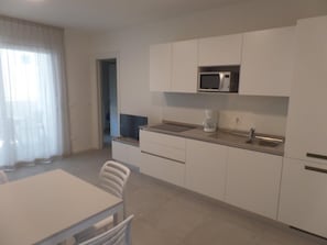Eine moderne Küche mit weißen Schränken, einer Mikrowelle, einer Kaffeemaschine und einem Essbereich mit Tisch und Stühlen.