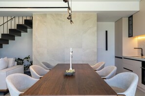 Ein moderner Essbereich mit einem Holztisch, sechs Stühlen, einer Blumenvase, einer Treppe und einer Küchenzeile.