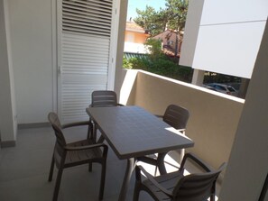 Ein Balkon mit Tisch und Stühlen, ein Fenster mit Blick auf Häuser und eine Tür mit Jalousien.