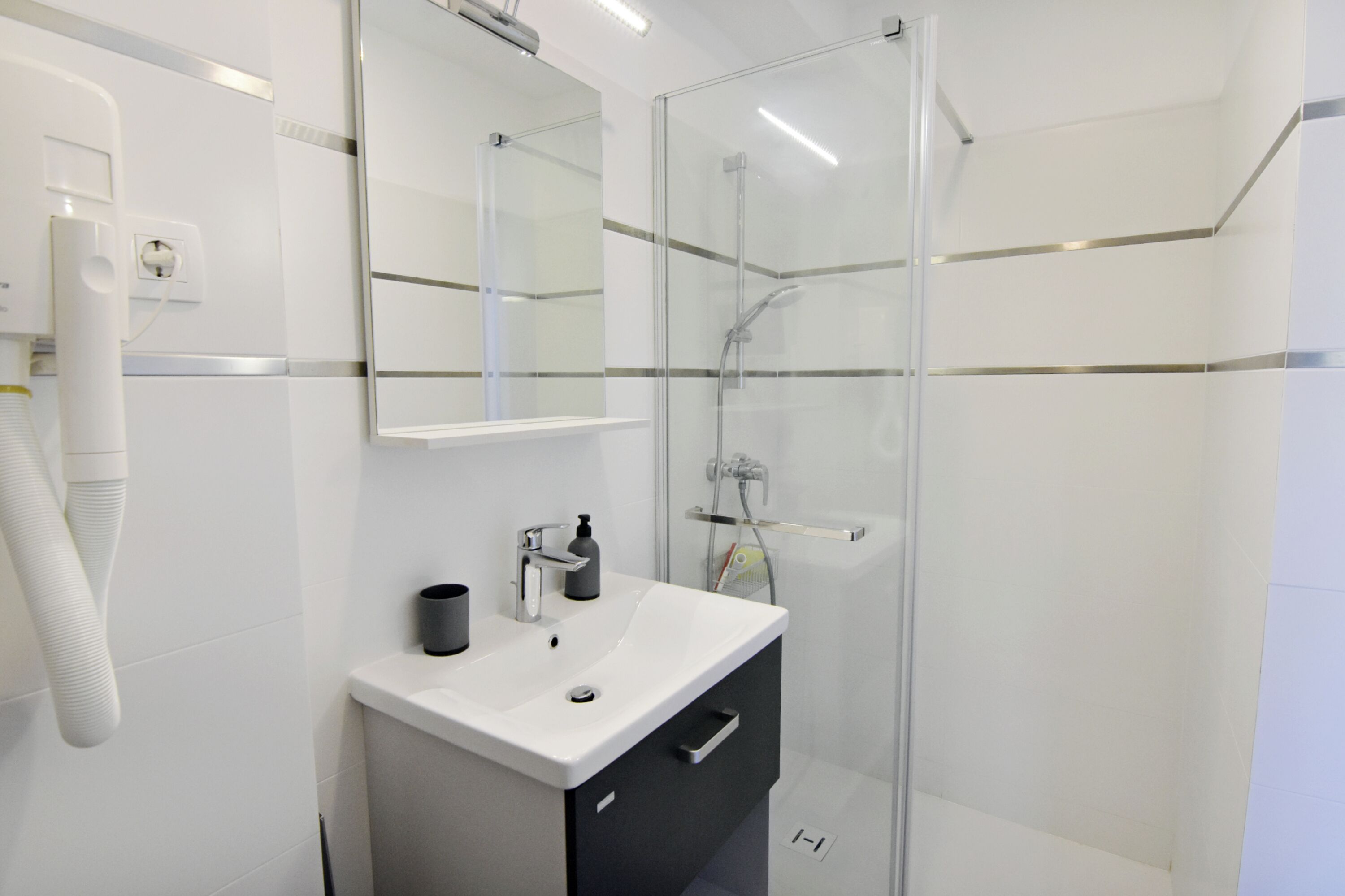 Een moderne badkamer met een glazen douchecabine, een wit wastafelmeubel met een zwart kastje, en een spiegel boven de wastafel.