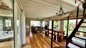 Ampla sala de estar com piso de madeira, um sofá, uma mesa de jantar e uma escada.