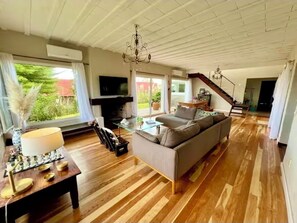 A spacious living room with a sofa, a television, a chandelier, and a staircase leading to another level. - Magnificent Views and Comfort in Punta Colorada (Punta Colorada)