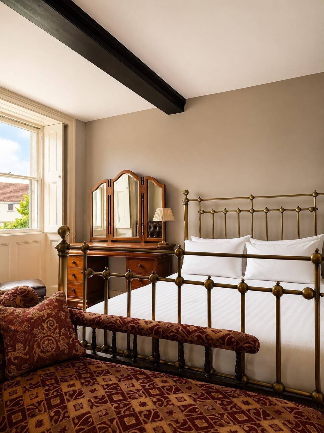 Une chambre à coucher comprenant un lit, un banc, une commode et un miroir.