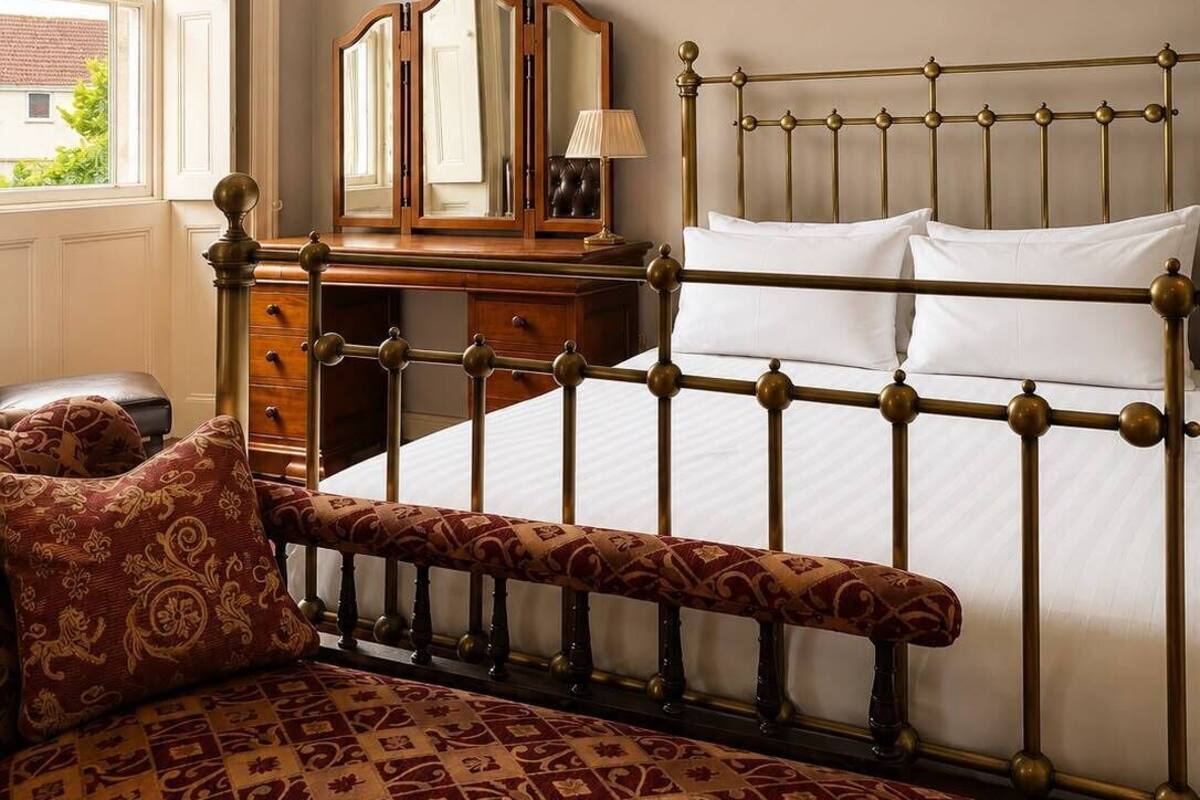 A bedroom with a bed, a bench, a dresser, and a mirror.