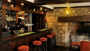 A bar area with a stone wall, bar stools, and a fireplace.