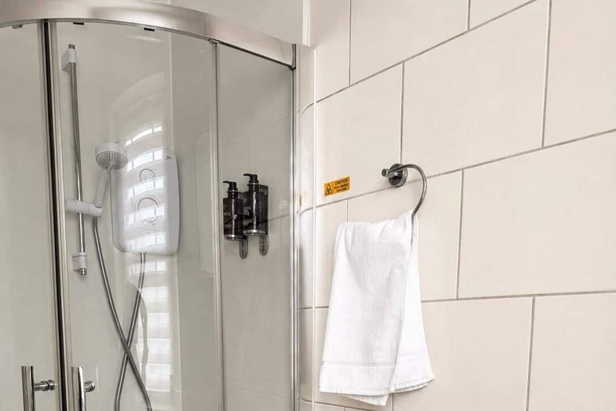 A glass-enclosed shower with a handheld showerhead, a wall-mounted faucet, and a tiled floor.