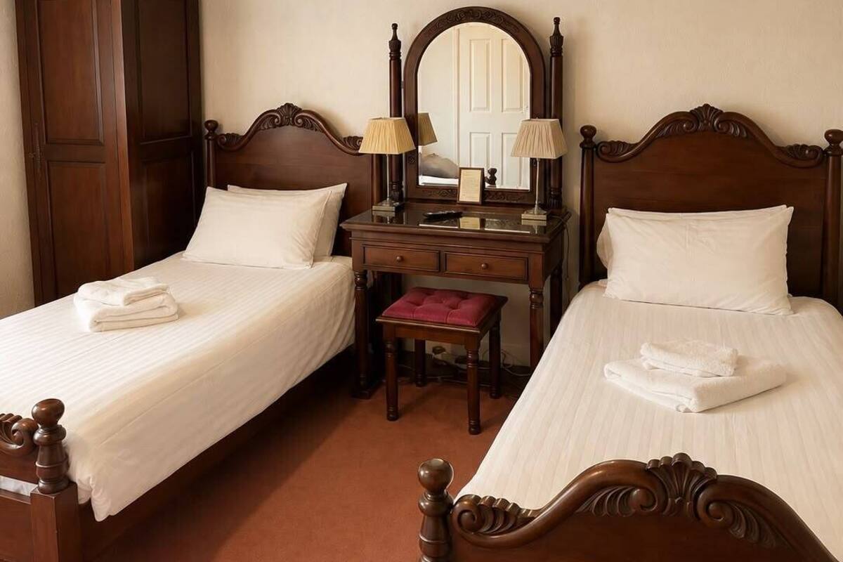 A hotel room with two beds, a desk, a mirror, and a wardrobe.