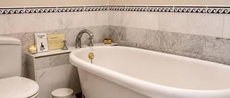 A bathroom with a white bathtub, a toilet, and a trash can.