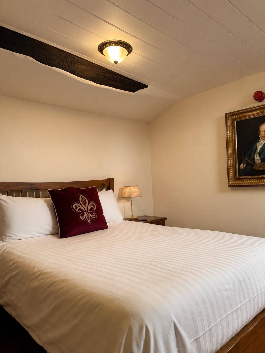 Une chambre d’hôtel avec un grand lit, une tête de lit en bois, une table de chevet avec une lampe et un portrait encadré accroché au mur.