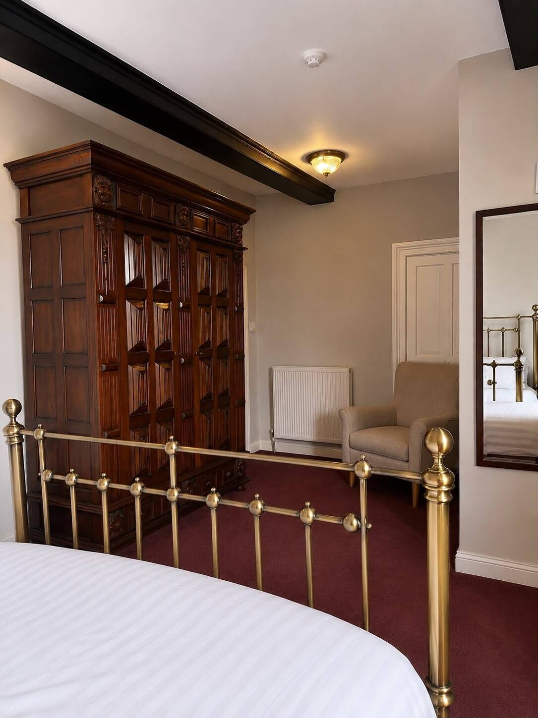 Ein Schlafzimmer mit einem Bett, einem Holzschrank, einem Heizkörper, einem Sessel und einem Spiegel an der Wand.