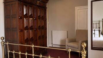 A bedroom with a bed, a wooden wardrobe, a radiator, a chair, and a mirror on the wall.