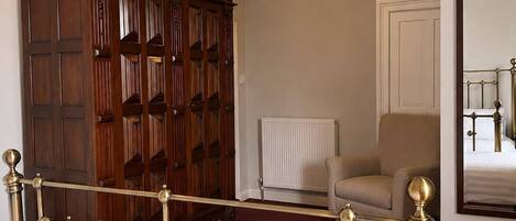 Une chambre à coucher avec un lit, une armoire en bois, un radiateur, une chaise et un miroir au mur.