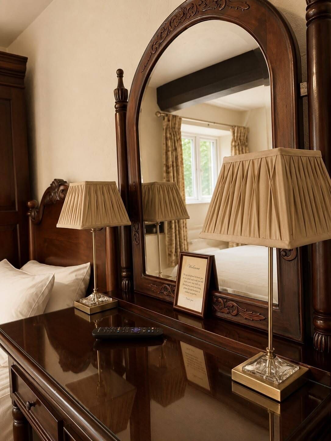 Een houten dressoir met twee lampen, een spiegel en een bord met een welkomstboodschap in een hotelkamer.