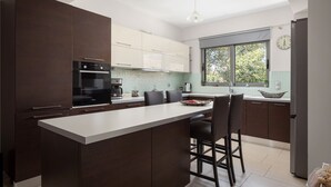 Eine moderne Küche mit einer zentralen Kochinsel, dunklen Schränken, einem eingebauten Backofen und einem großen Fenster.