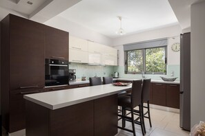 Uma cozinha moderna com ilha central, armários escuros, forno embutido e uma janela ampla.